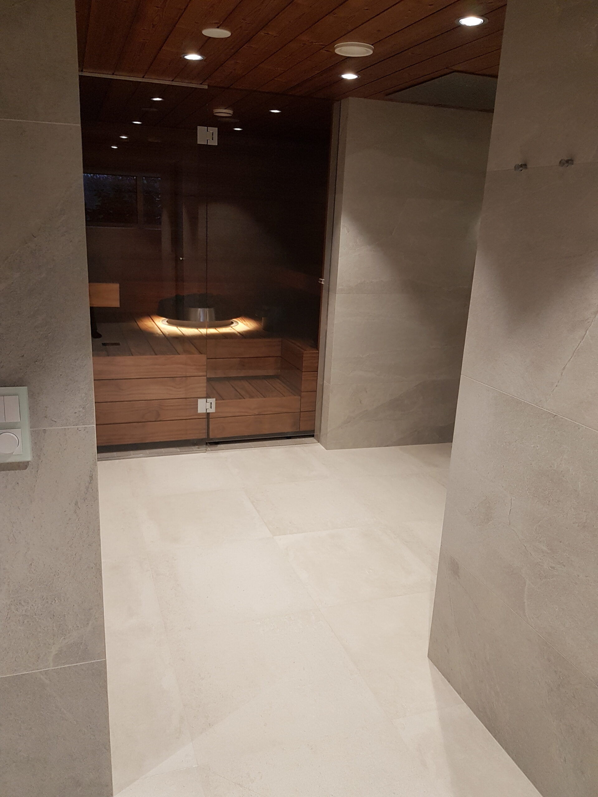 Heledate suurplaatidega viimistletud vannituba koos klaasukse ja puidust saunasisustusega – modernne lahendus NewTiling sauna- ja märgruumide renoveerimisel.